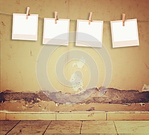 Old polaroid photo frames hanging on a rope over textured grunge wall and floor pattern