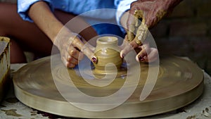 Old potter guides lady fingers making clay pot on wheel