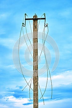 Old power line post with ripped electric wires hanging on it on the blue sky background