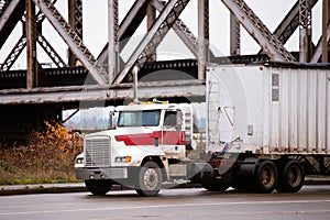 Old powerful bonneted truck with bulk trailer under bridge