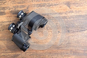 Old prism black color binoculars over wooden background closeup