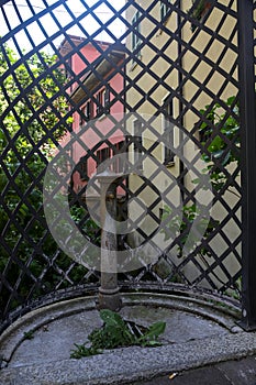 Old public fountain in front of a fence with a row of houses