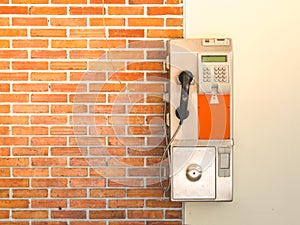 An old public payphone with red brick wall.