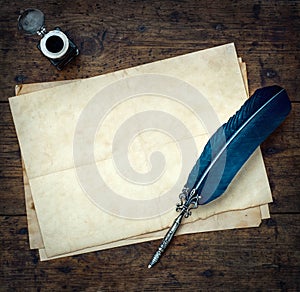 Old quill pen, and old paper blank sheet and vintage inkwell on wooden desk in the old office . Retro style. Conceptual background photo