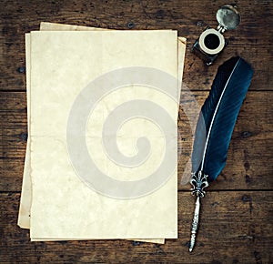 Old quill pen, and old paper blank sheet and vintage inkwell on wooden desk in the old office . Retro style. Conceptual background photo