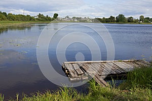 An old raft for a fisherman on the shore of a calm blue lake in the summer.