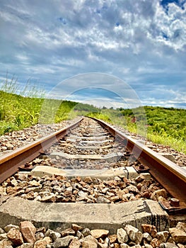 Old railroad surrounded by bright green grass under a sunny sky full of clouds