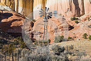 Old ranch windmill and fence in front of colorful high cliffs in the desert landscape of the American Southwest