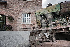 Old rasty tracked tractor in front of brick building
