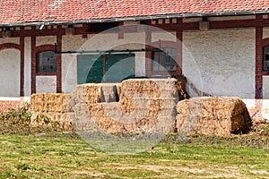 Old rectangular hay bales stored in front of abandoned farm building