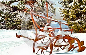 Old, red agricultural tiller, rusting in a cold, snowey field