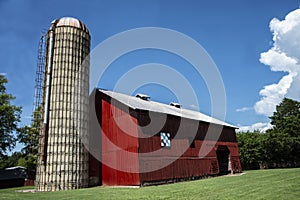 An old red barn with a huge silo sits in green grass.