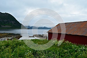 Old red boat house with cloudy mountain range background and small docked boat