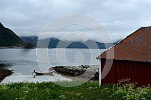 Old red boat house with cloudy mountain range background and small docked boat