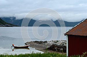 Old red boat house with cloudy mountain range background and small docked boat