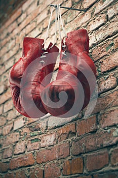 Old red boxing gloves hang on nail on brick wall with copy space for text. High resolution 3d render