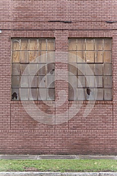 Old red brick building showing signs of abandonment with two busted windows.