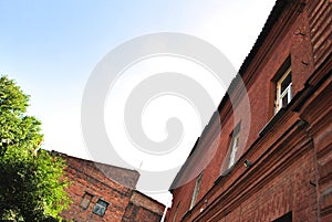 Old red brick building walls with windows, green trees, view from ground on slate roof, blue sky