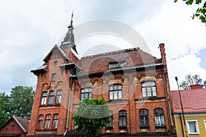 An old red brick house. Part of the red brick wall, windows and a fragment of the roof of an old residential building against the