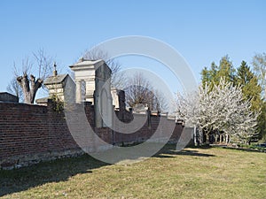 Old red brick wall of country cemetery at village Cvikov in luzicke hory, Lusatian Mountains, spring trees, blue sky