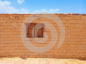 Old red brick wall with old wooden window under blue sky in desert landscape. Constructions and architecture of the Egyptian