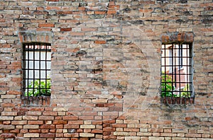 Old red brick wall with two rusted iron grill windows