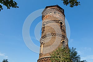 Old red brick water tower with windows of different sizes against a blue sky