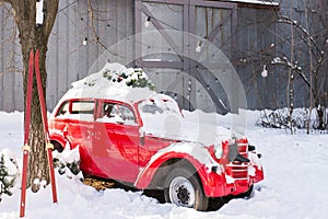 Old red car with Christmas tree branches on the roof in the snow-covered yard