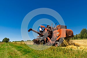 Old red combine harvester working in a wheat field