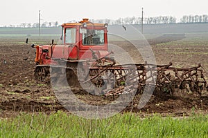 An old red crawler tractor plows a field. Green grass in the foreground