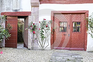 Old red doors with wrought iron details and colorful rose plant