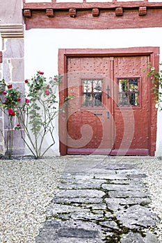 Old red doors with wrought iron details and colorful rose plant