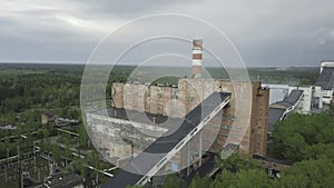 Old red industrial factory building with tall smokestack against grey rainy sky. Aerial view