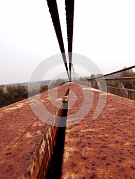 Old red iron stripes of the handrail, steel cables, construction of a metallic rusty bridge