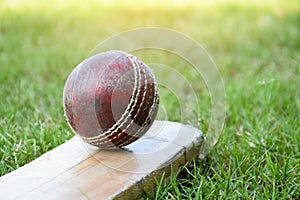 An old red leather cricket ball on bat