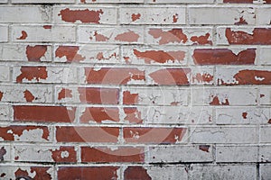 Old red shabby damaged brick wall with gray cement, stains of white, black paint and cracks. rough surface texture