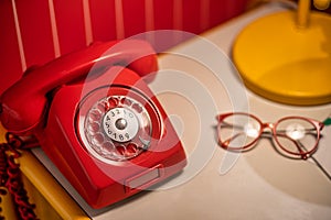 Old red telephone with rotary dial on the table with old glasses