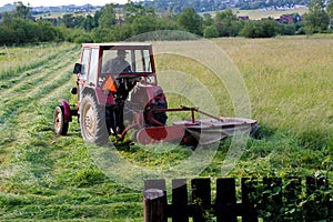 Old red tractor, cutting up hay in a field