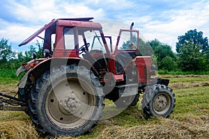 Old red tractor in the field during the haymaking season, pressing hay on bales, forage harvesting