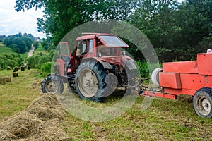 Old red tractor in the field during the haymaking season, pressing hay on bales, forage harvesting