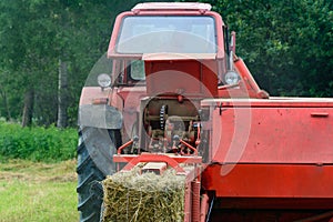 Old red tractor in the field during the haymaking season, pressing hay on bales, forage harvesting