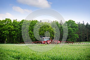 Old red tractor spraying fertilizer or herbicide on a field near