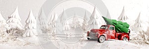 Old red truck transporting green Christmas tree in white snowy forest