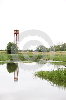 Old red water tank in the field with a reflection in the pond