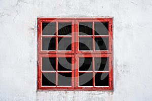 Old red weathered window with squares on white wall with worn texture.