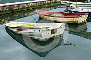 Old red and white boats moored with ropes in the harbor. Sea water with seaweed and raindrops. A beautiful reflection.