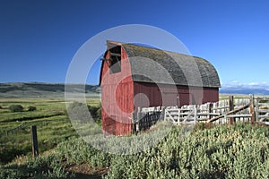 Old red wooden building in Montana USA with roof in form of arc and a fence around