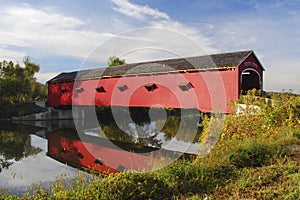 Old red wooden covered bridge reflecting in calm river