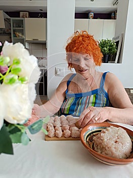 Old redheaded woman making food, cooking meat. 70 years old