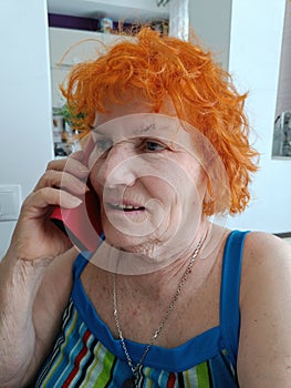 Old redheaded woman is speaking on smartphone. Happy and smiling